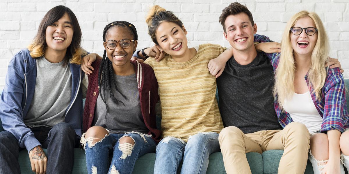 Five smiling teens sitting with arms around each other