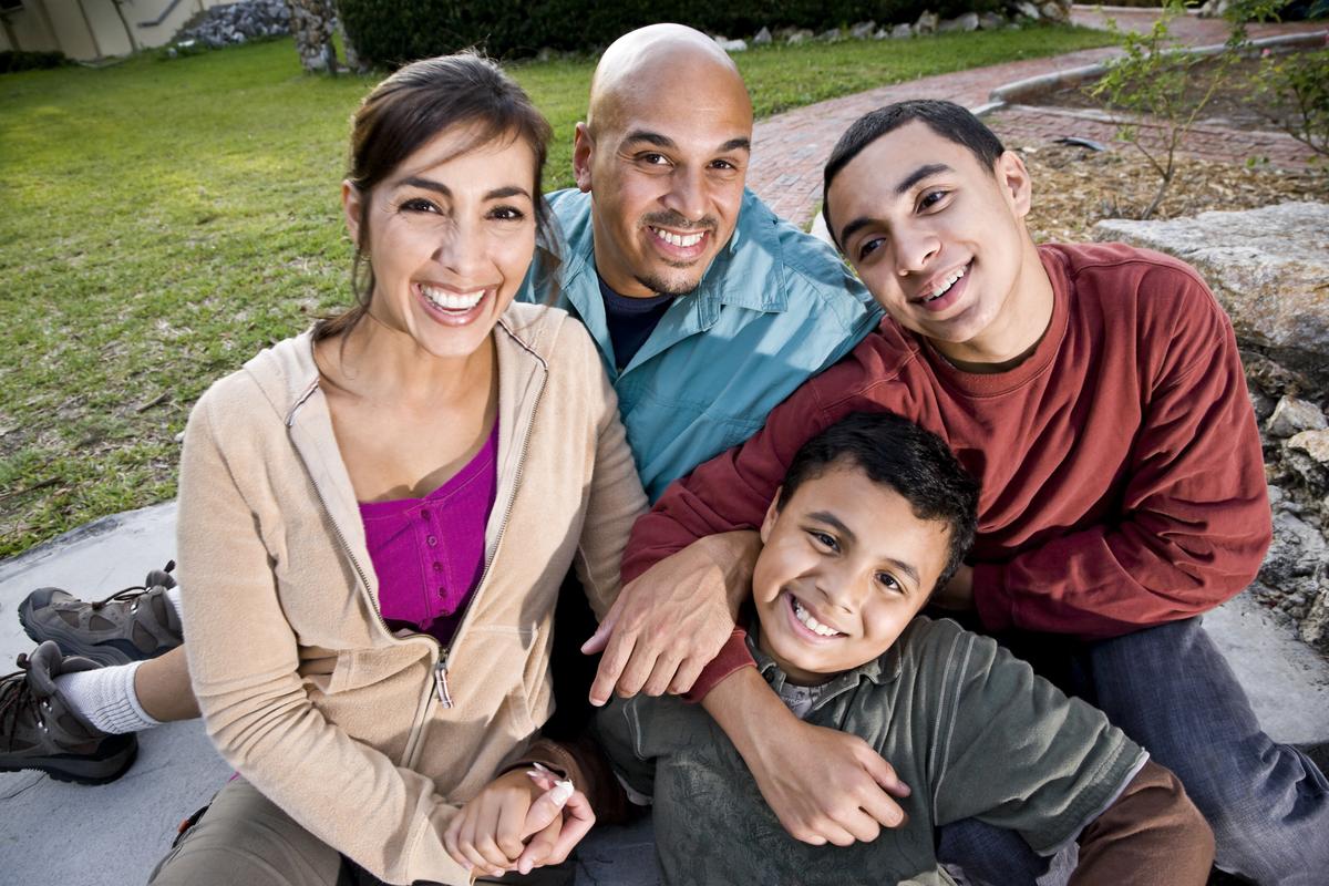 Hispanic mother, father, and two smiling teens sitting outside
