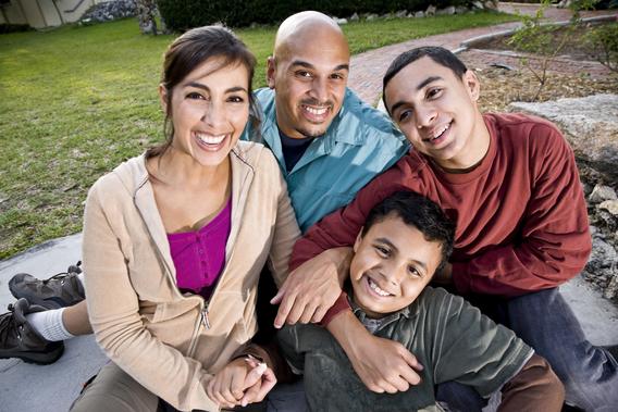 Hispanic mother, father, and two smiling teens sitting outside